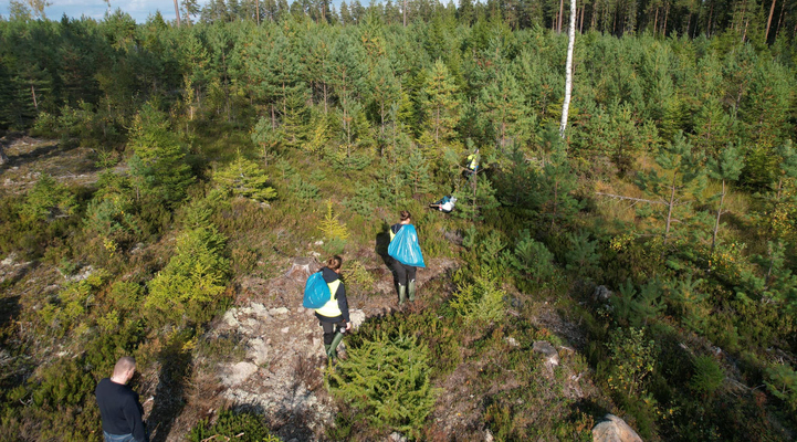 Bild uppifrån på människor som går i skogen med blåa plastsäckar på ryggen