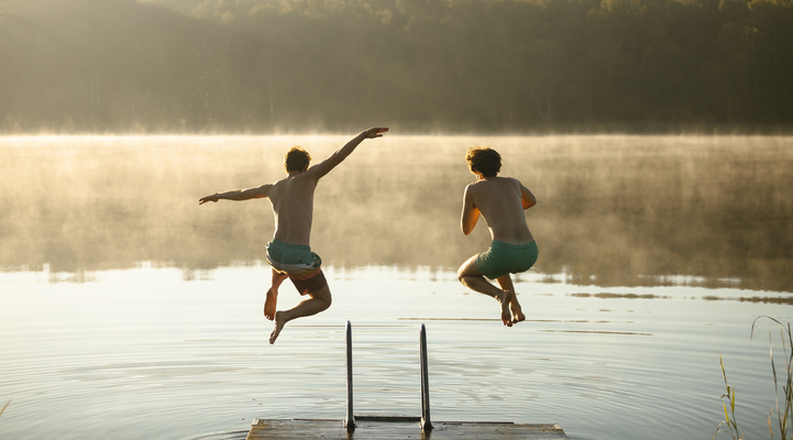 Två män hoppar från brygga i sjö