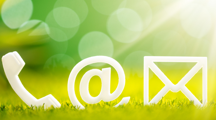 Symboler på en telefon, snabel-a och ett kuvert som ligger i grönt gräs