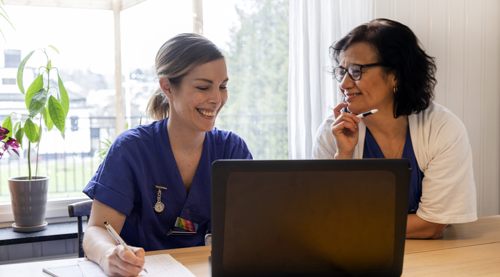Bild på två glada kvinnor inom vården framför en dator