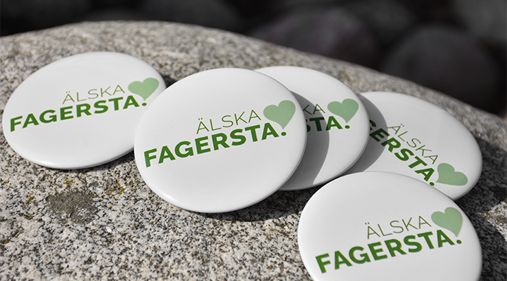 Fem vita reklamknappar med Fagerstas platsvarumärke på. Knapparna ligger på en sten.