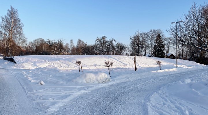 Vinterbild med snöbeklädd mark. En väg som delar sig åt två olika håll och rakt fram syns en kulle där Trygghetsboendet planeras att byggas.