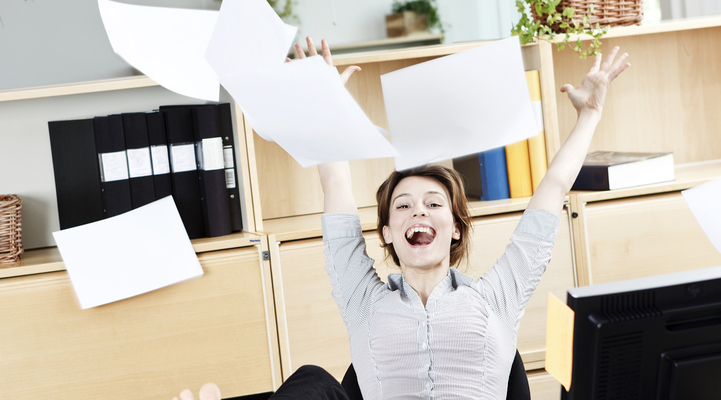 Bild på en kvinna som sitter vid ett skrivbord och kastar papper upp i luften