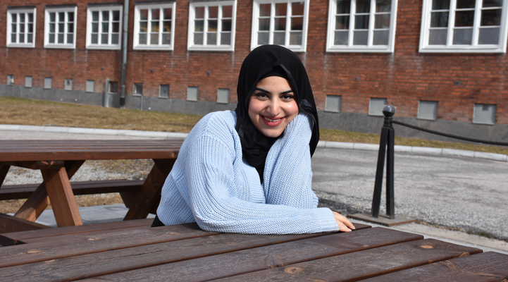 Aya Elturk sitter utanför Fagersta kommunhus på en träbänk och har ena armbågen på bordet och handen som stöd under hakan.