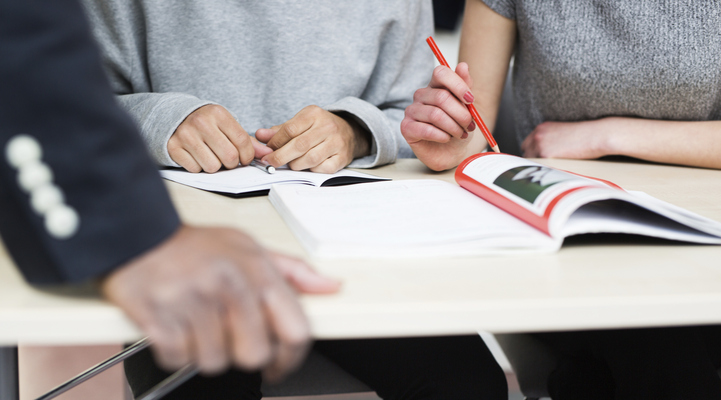 Två elever sitter vid en bänk och pluggar. En tredje persons hand håller i kortsidan av bordet.