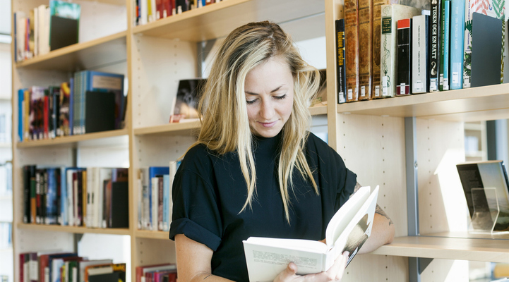 Kvinna står och läser i en bok på ett bibliotek.