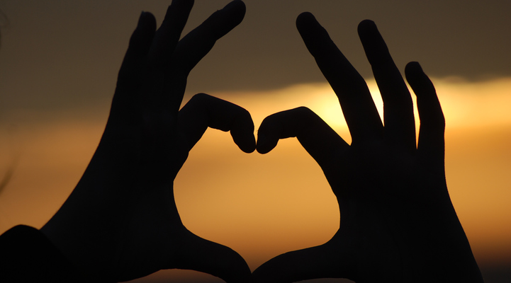 Två händer som bilder ett hjärta med en solnedgång i bakgrunden