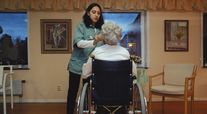 Vårdpersonal som sköter om en äldre kvinna i rullstol.