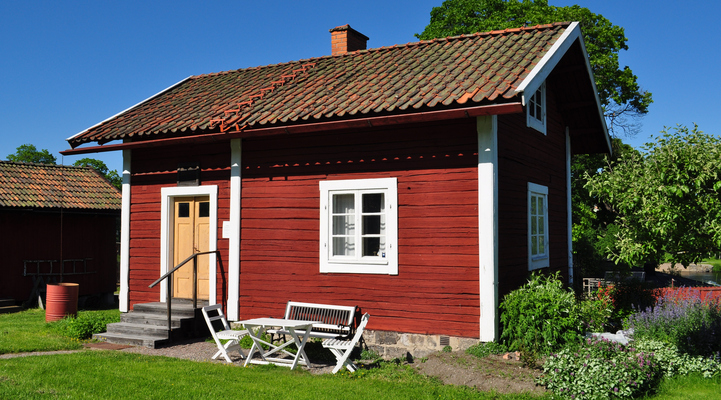 Soldattorpet på hembygdsgården. En röd stuga med vita knutar, gul dörr. Framför huset står vita trädgårdsmöbler.
