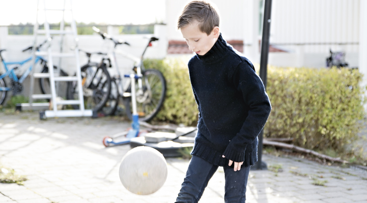 Pojke spelar fotboll utanför carport