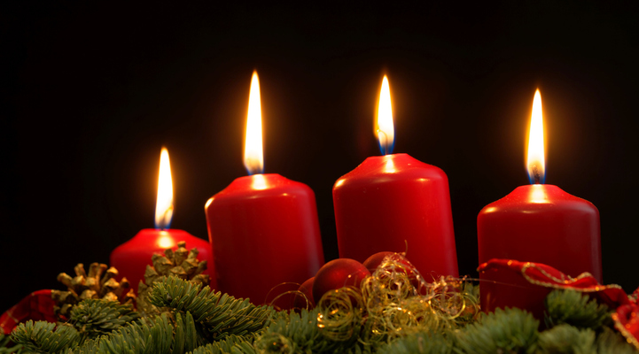 Red candles of an Advent wreath with fir branches and a black background.