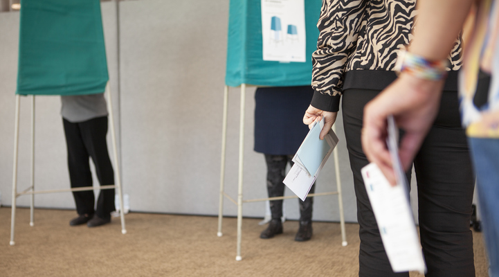 Två personer står i kö med sina röstkort till valbåsen.